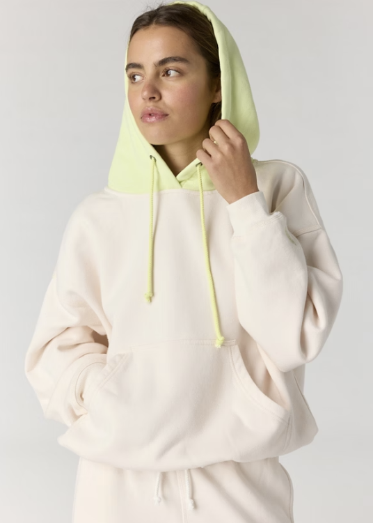 Woman wearing cream hoodie with yellow hood on plain background