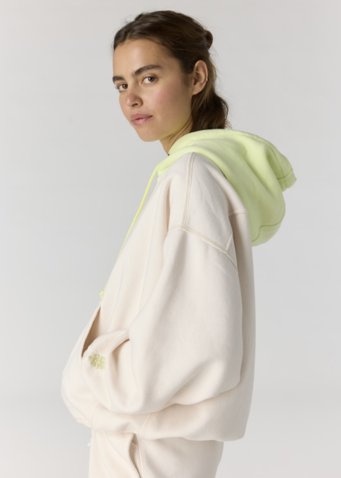 Woman wearing cream hoodie with yellow hood on plain background