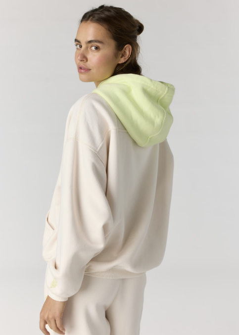 Woman shown from back wearing beige hoodie with yellow hood on plain background
