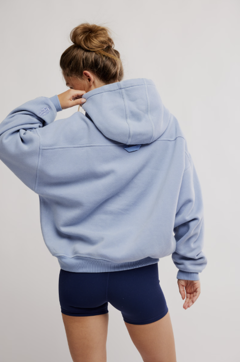 Person wearing a light blue hoodie and dark shorts on a plain background