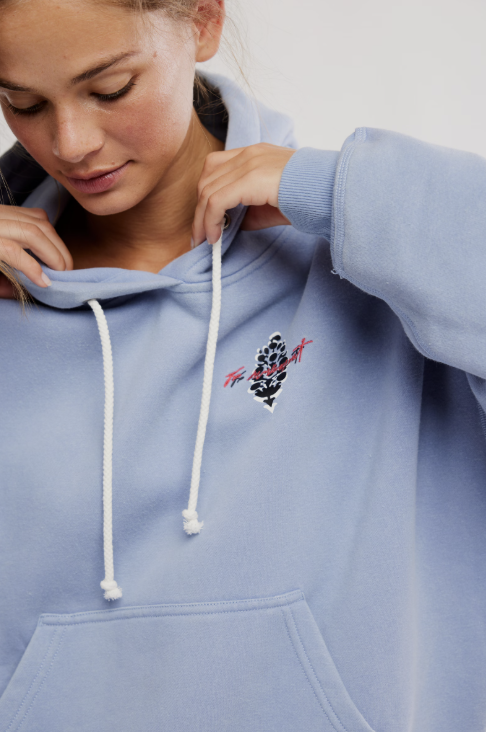 Person wearing a light blue hoodie with a logo on the chest against a plain background