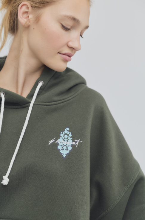 Person wearing a green hoodie with a logo on a plain background