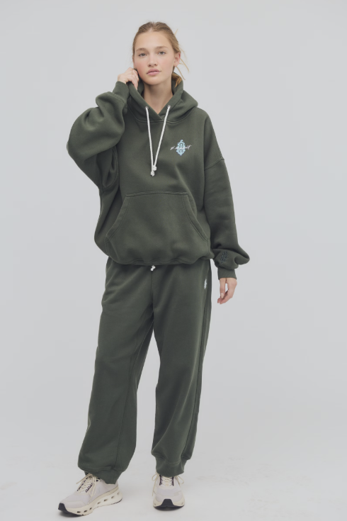 Person wearing a green tracksuit with a logo on a light gray background