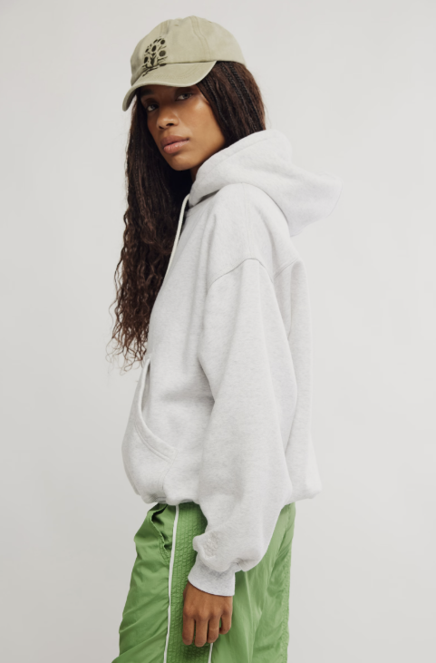 Person wearing a light gray hoodie and green pants with a beige cap on a white background