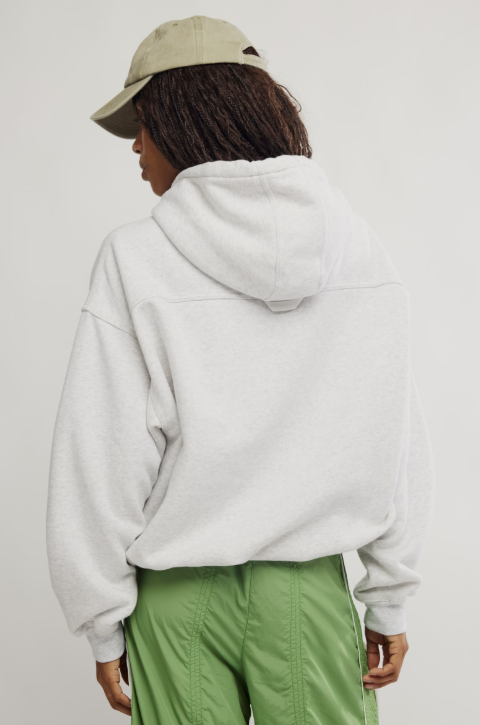 A person shown from the back wearing a light gray oversized hoodie, olive green pants, and a beige baseball cap against a plain light gray studio background.