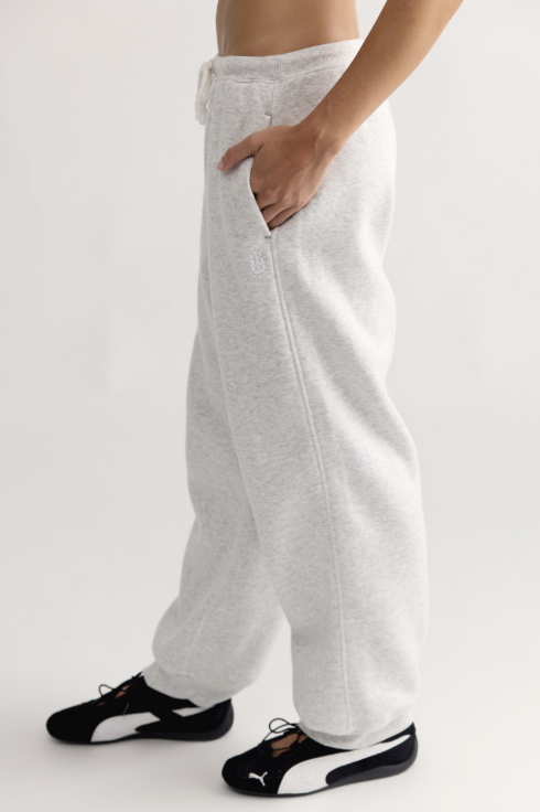 A person wearing light heather gray sweatpants with a side pocket and drawstring waist, paired with black and white Puma sneakers, shown from the waist down against a plain light background.