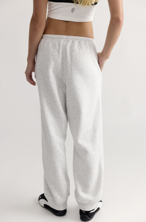 A person shown from the back wearing light heather gray sweatpants, a white cropped top, and black-and-white sneakers against a plain light gray studio background.
