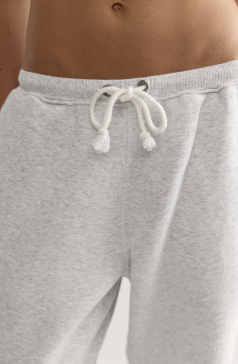 Close-up of a person wearing light heather gray sweatpants with a white drawstring at the waistband.