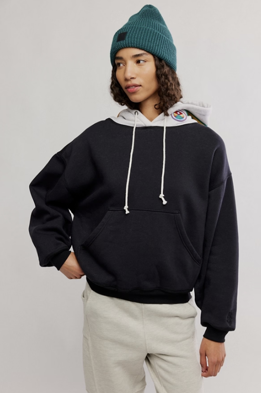 Person wearing a black hoodie, white beanie, and light gray pants on a plain background