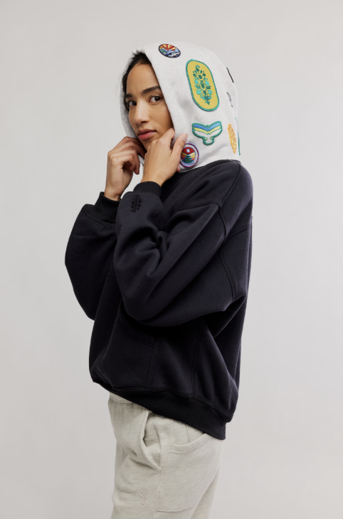 Person wearing a black hoodie with colorful patches on a plain background