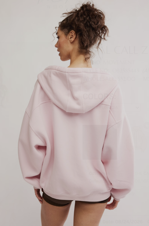 A woman shown from the back wearing an oversized light pink hoodie, photographed against a plain light gray studio background.