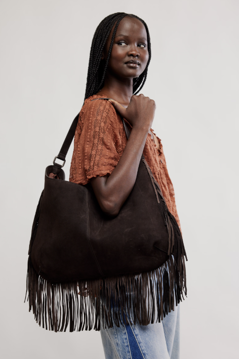 Woman holding a brown leather handbag with fringes against a plain background