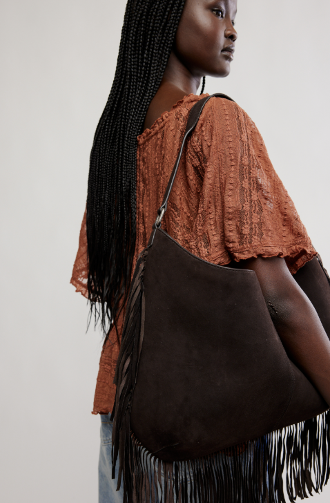 Woman carrying a brown leather handbag with fringe details on a plain background