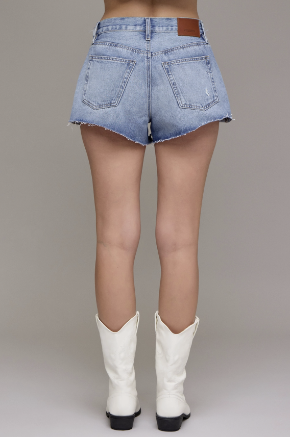 Person wearing light blue denim shorts and white cowboy boots on a plain background