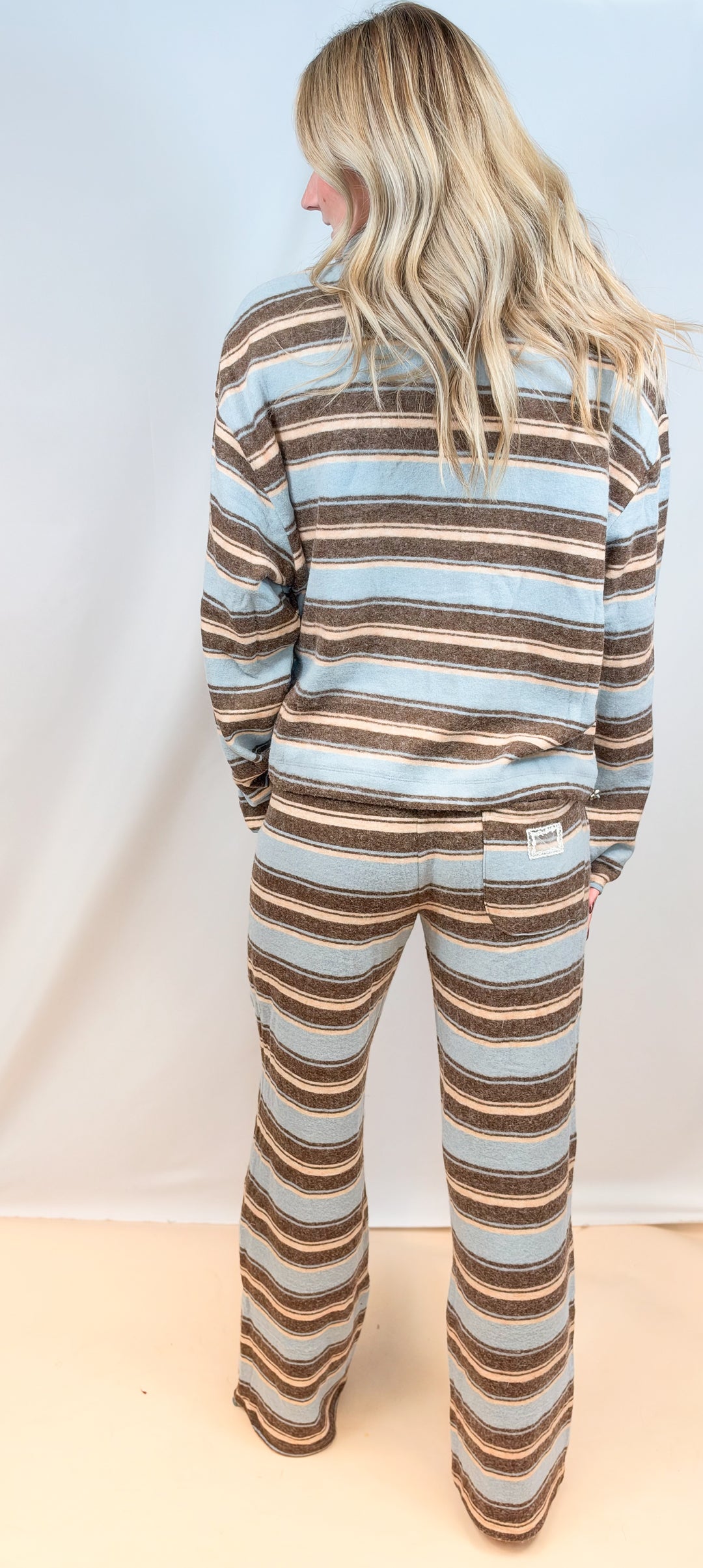 Woman shown from back view wearing light blue and brown stripe matching set on plain background