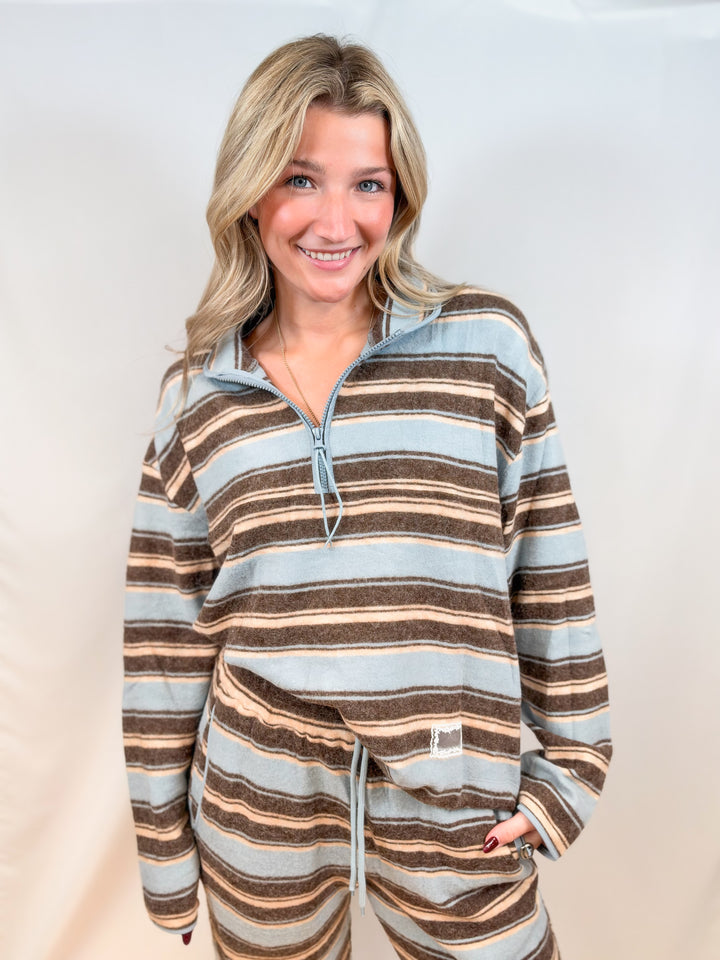 Woman wearing light blue and brown stripe quarter zip top and pants on plain background