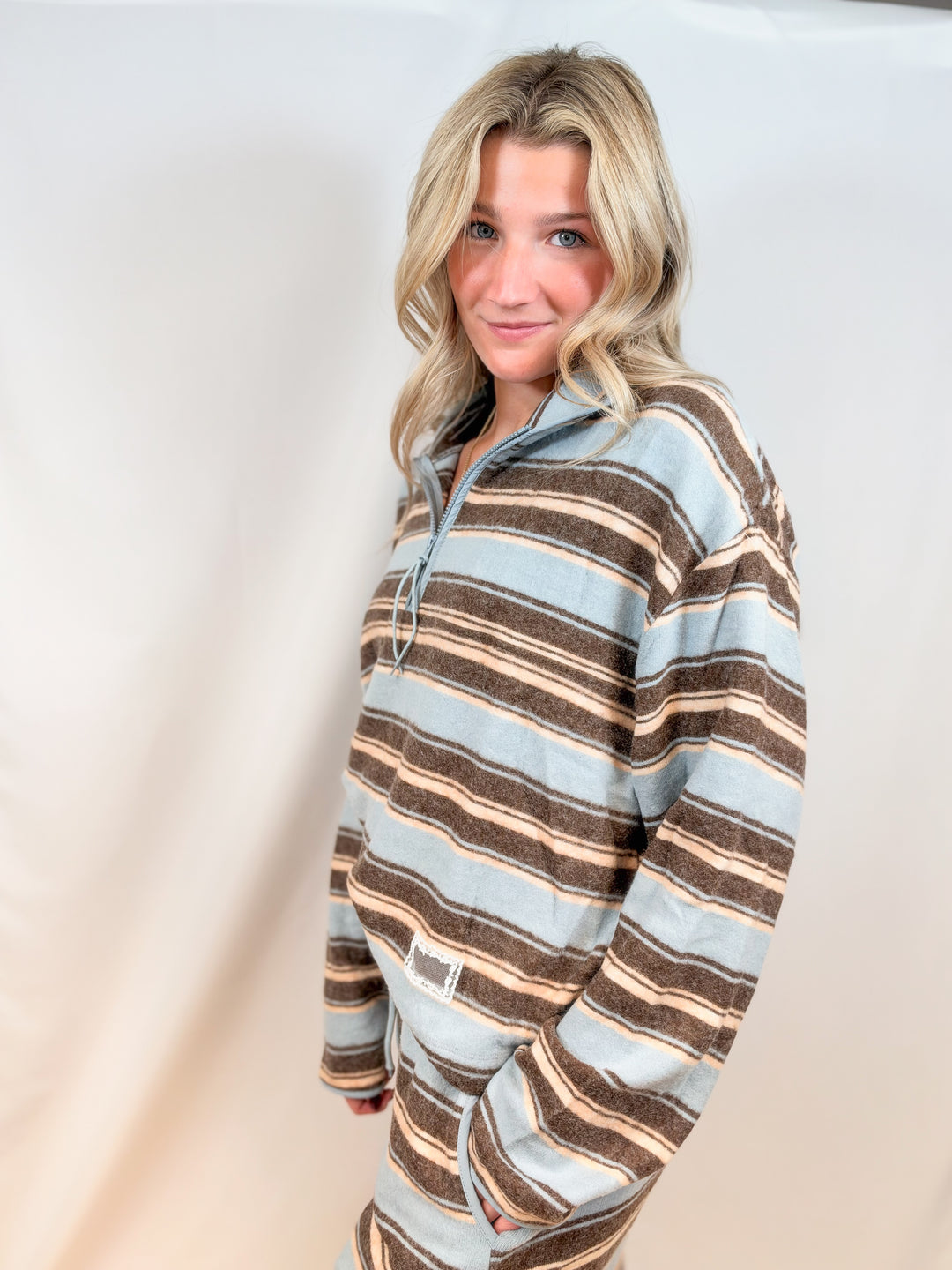 Woman wearing matching light blue and brown stripe set with quarter zip and pants on plain background