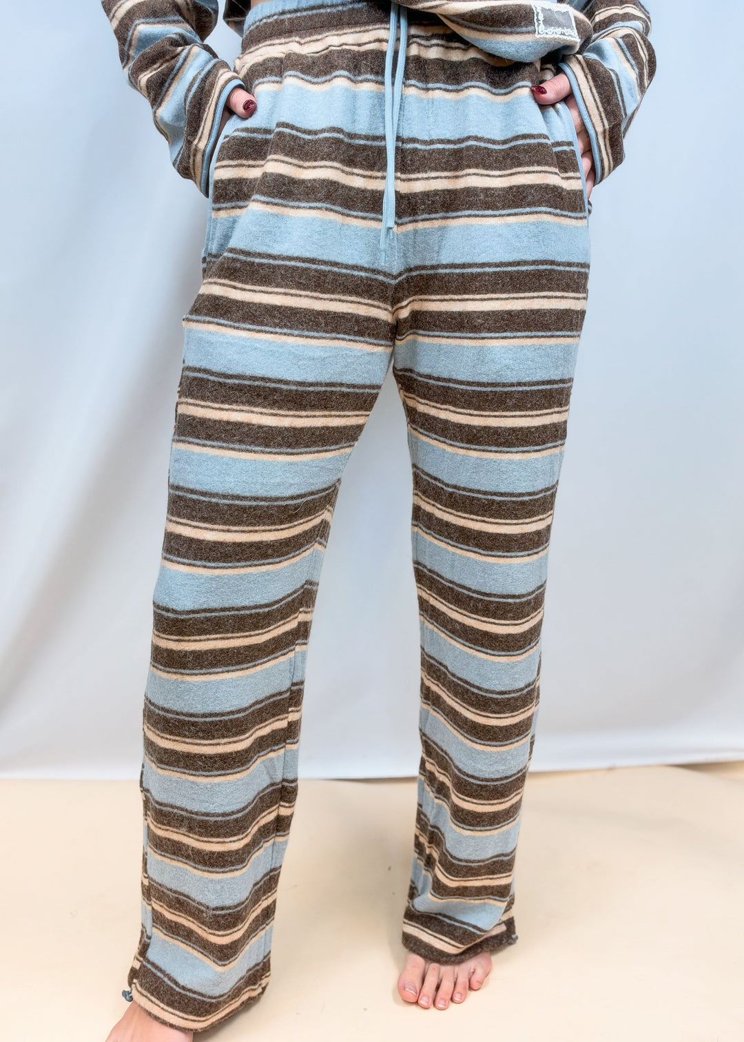 Woman shown waist down wearing light blue and brown stripe pants on plain background