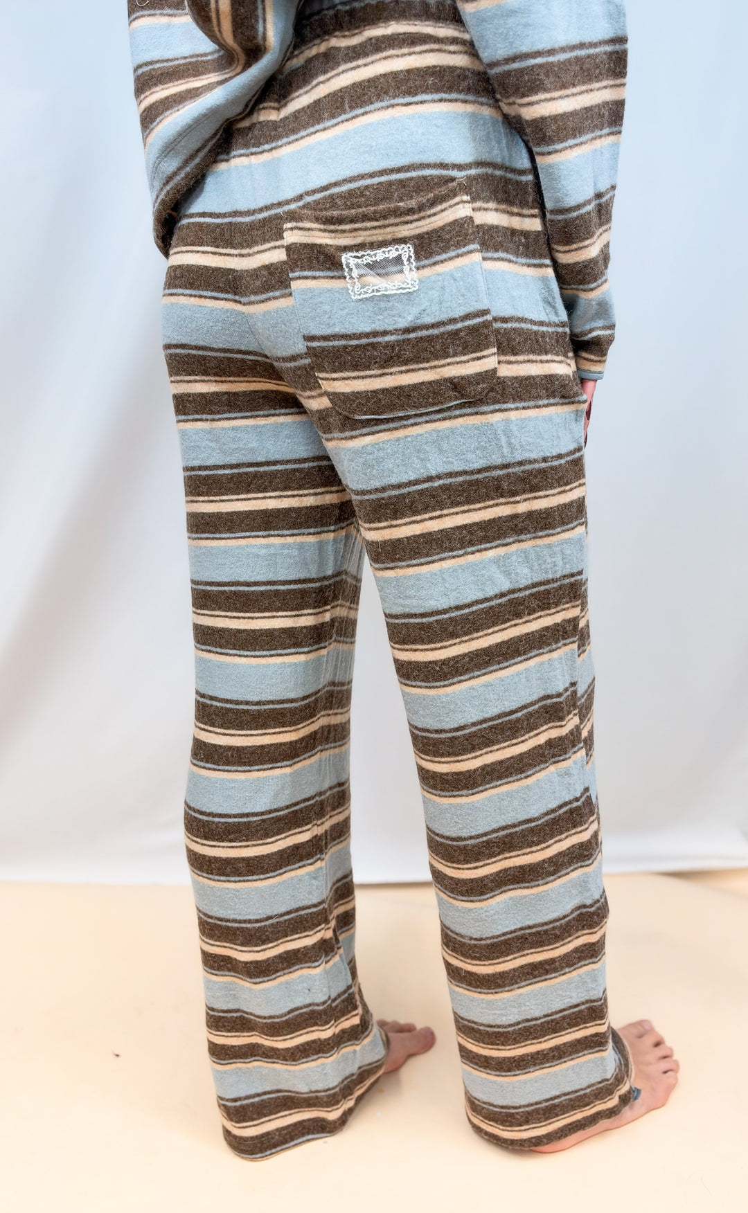 Woman shown from back view wearing light blue and brown stripe pants on plain backgorund
