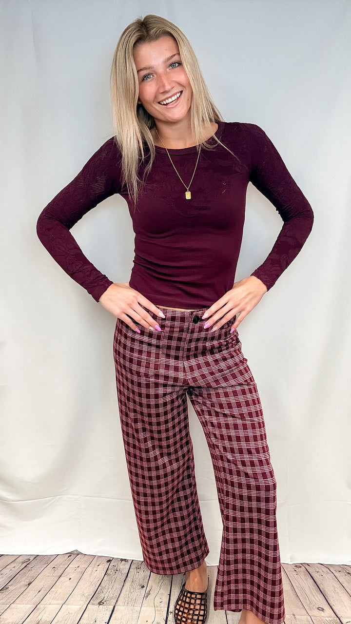 Woman wearing burgundy plaid pants with fitted burgundy top on white background with wooden floor