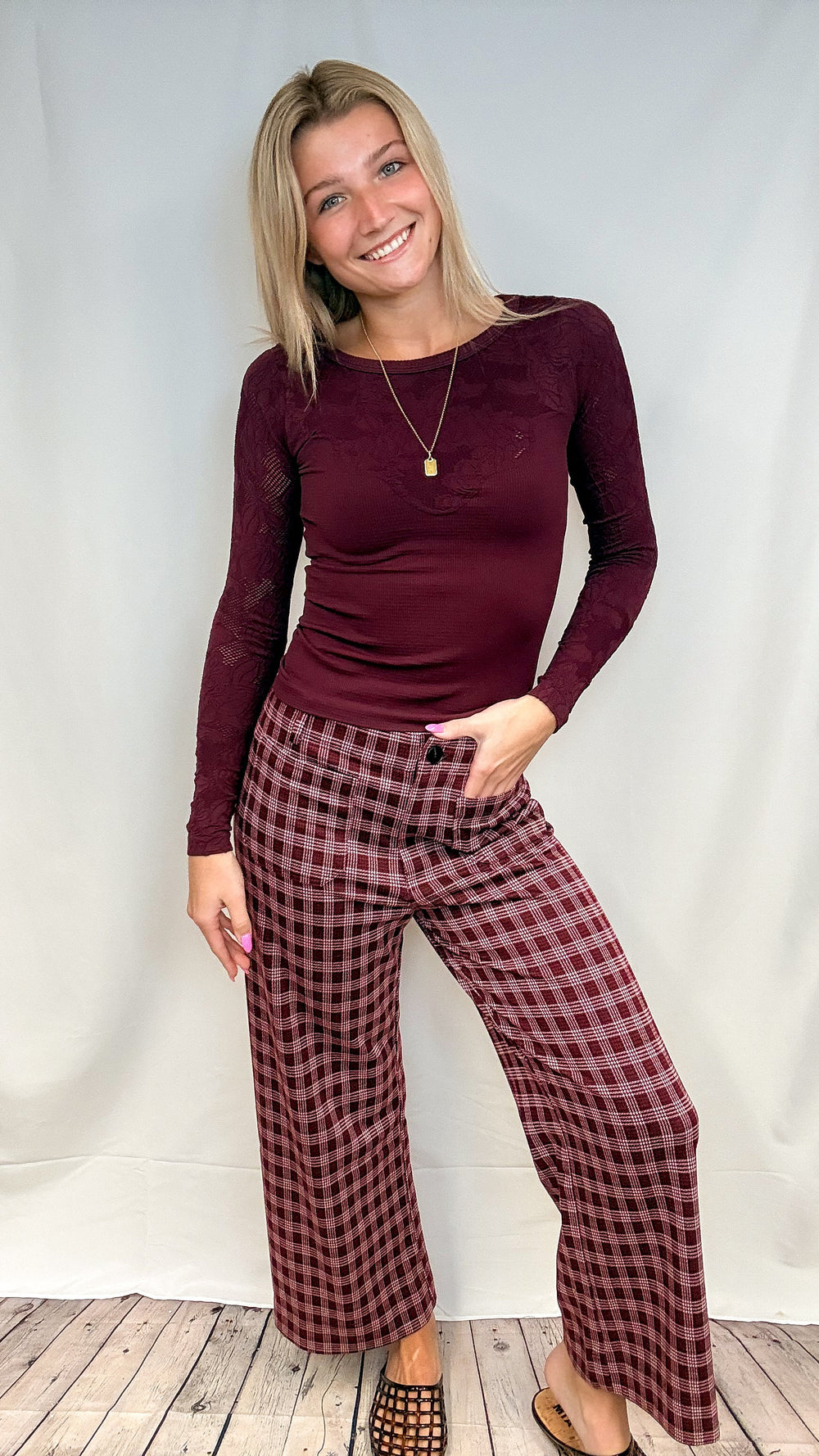Woman wearing burgundy plaid pants with fitted burgundy top on white background with wooden floor