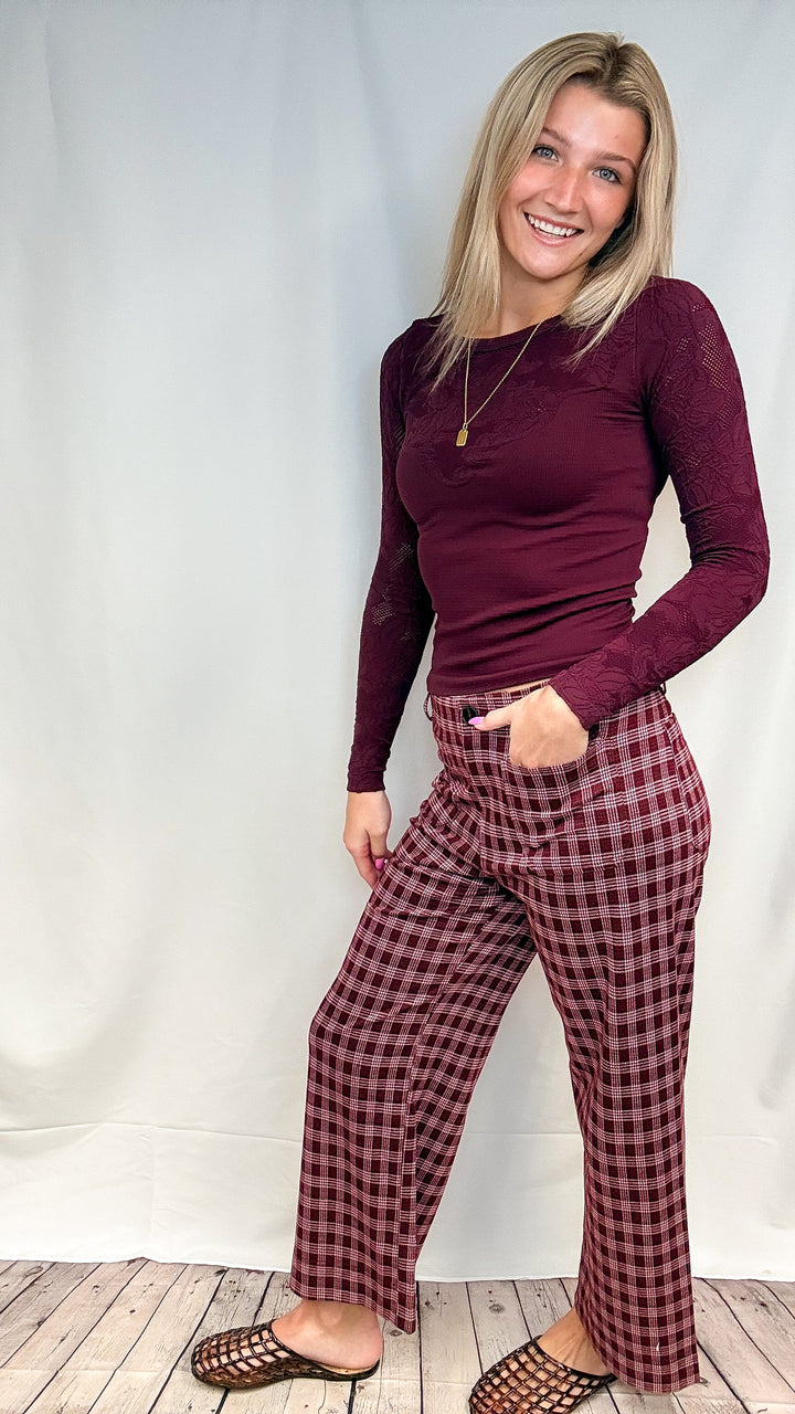 Woman wearing burgundy plaid pants with fitted burgundy top on white background with wooden floor