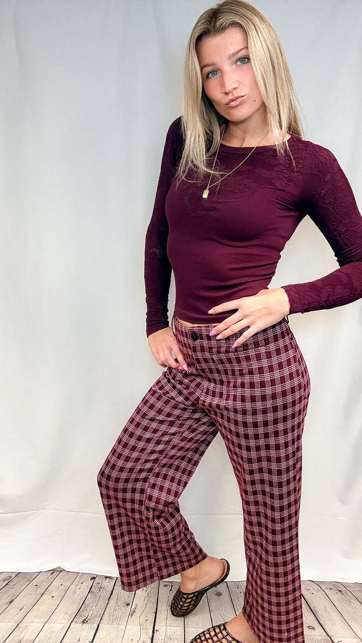 Woman wearing burgundy plaid pants with fitted burgundy top on white background with wooden floor