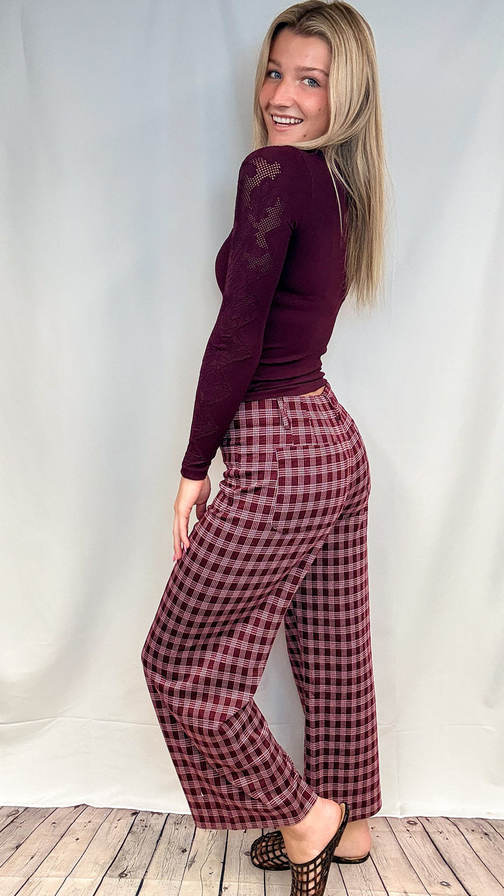 Woman wearing burgundy plaid pants with fitted burgundy top on white background with wooden floor