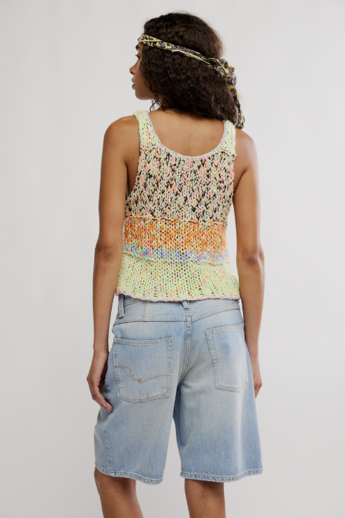 Woman wearing a colorful tank top and light blue shorts on a plain background