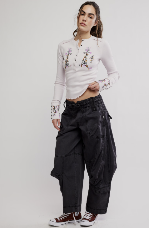 Woman wearing a white embroidered shirt and black pants on a white background