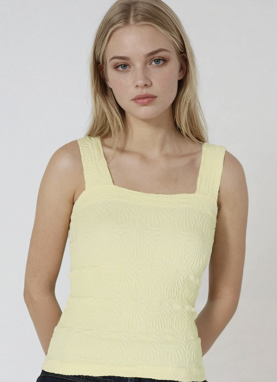 A blonde model wearing a pale yellow textured knit tank top with a square neckline, photographed against a light gray studio background.
