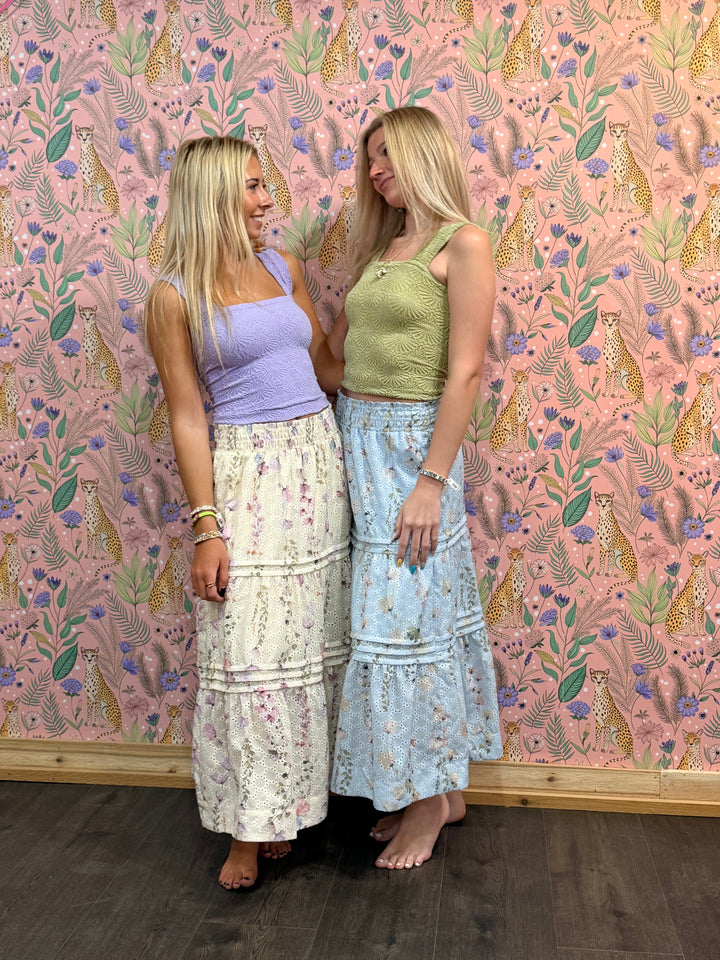 Two women standing against a pink floral-patterned wall.