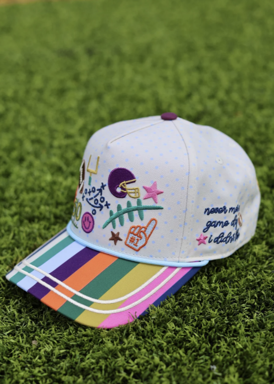 Trucker hat with football doodles and striped bill sitting on grass