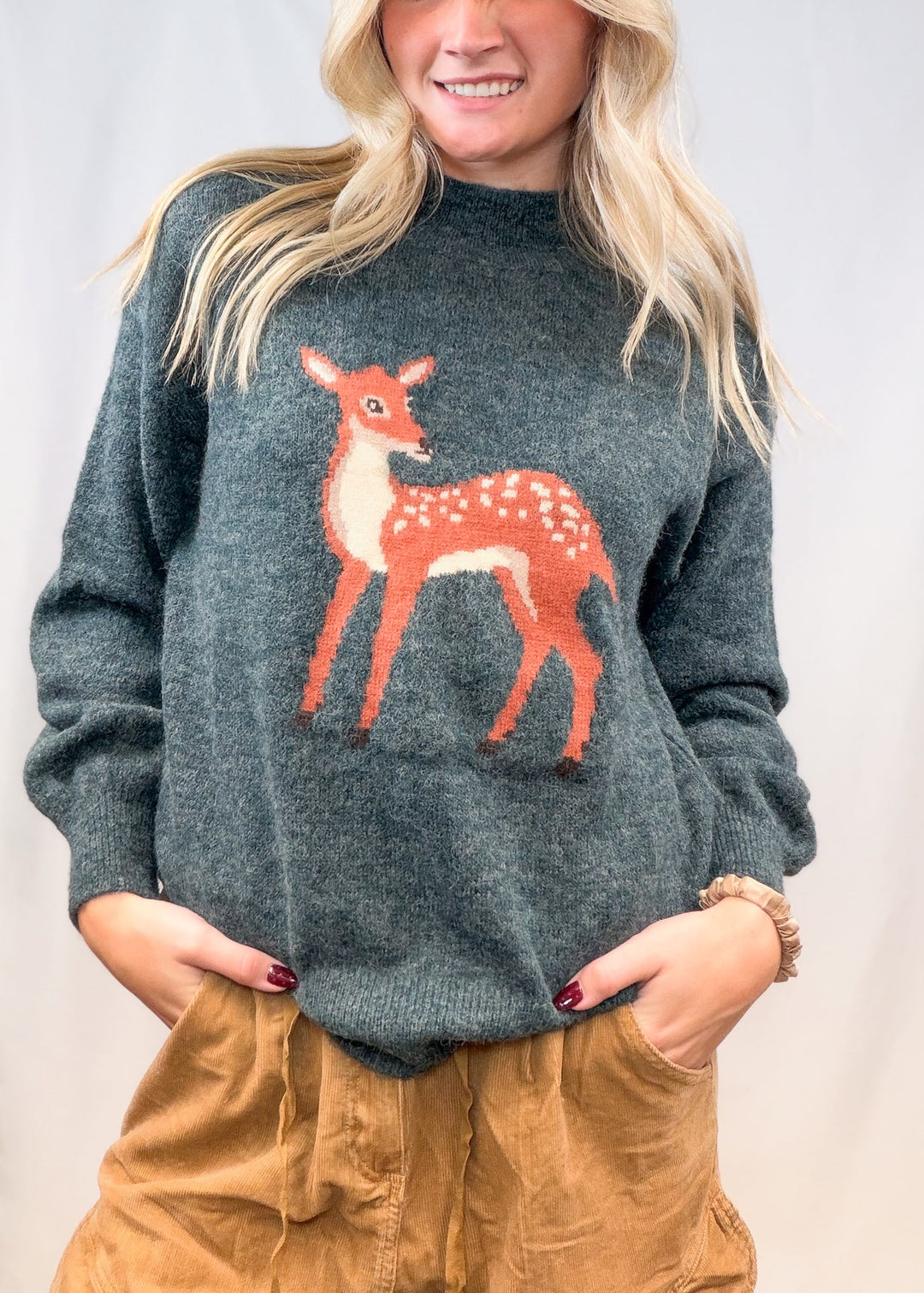 Woman wearing green sweater with fawn graphic on front on plain background