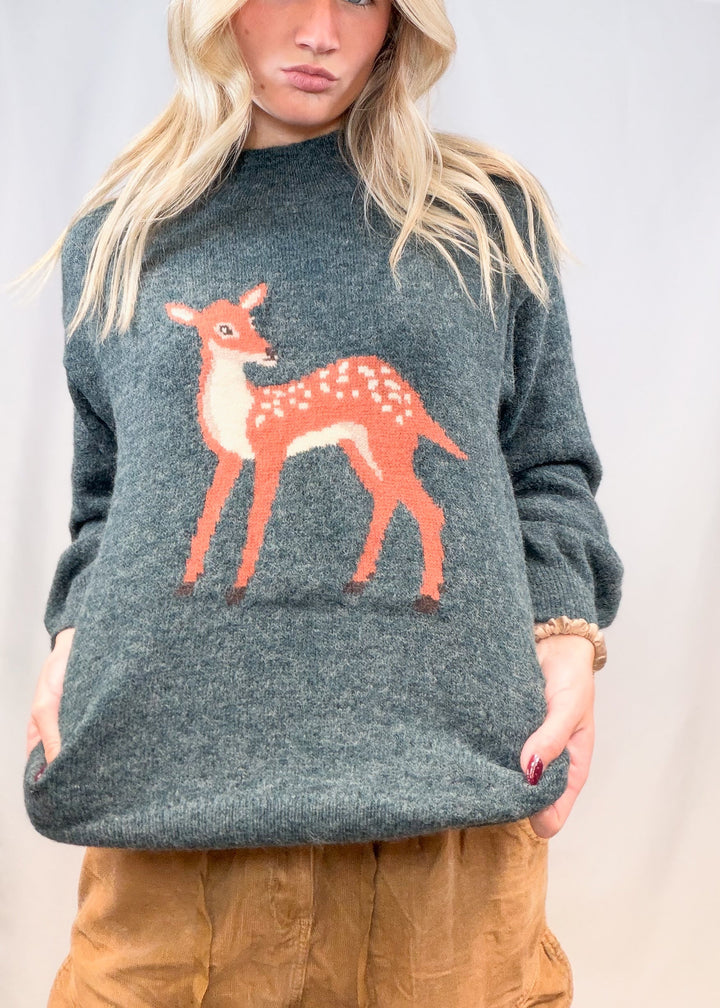 Woman wearing green sweater with fawn graphic on front on plain background