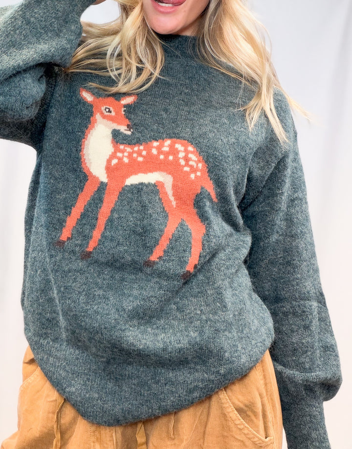Woman wearing green sweater with fawn graphic on front on plain background