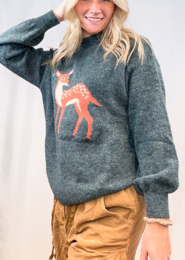 Woman wearing green sweater with fawn graphic on front on plain background