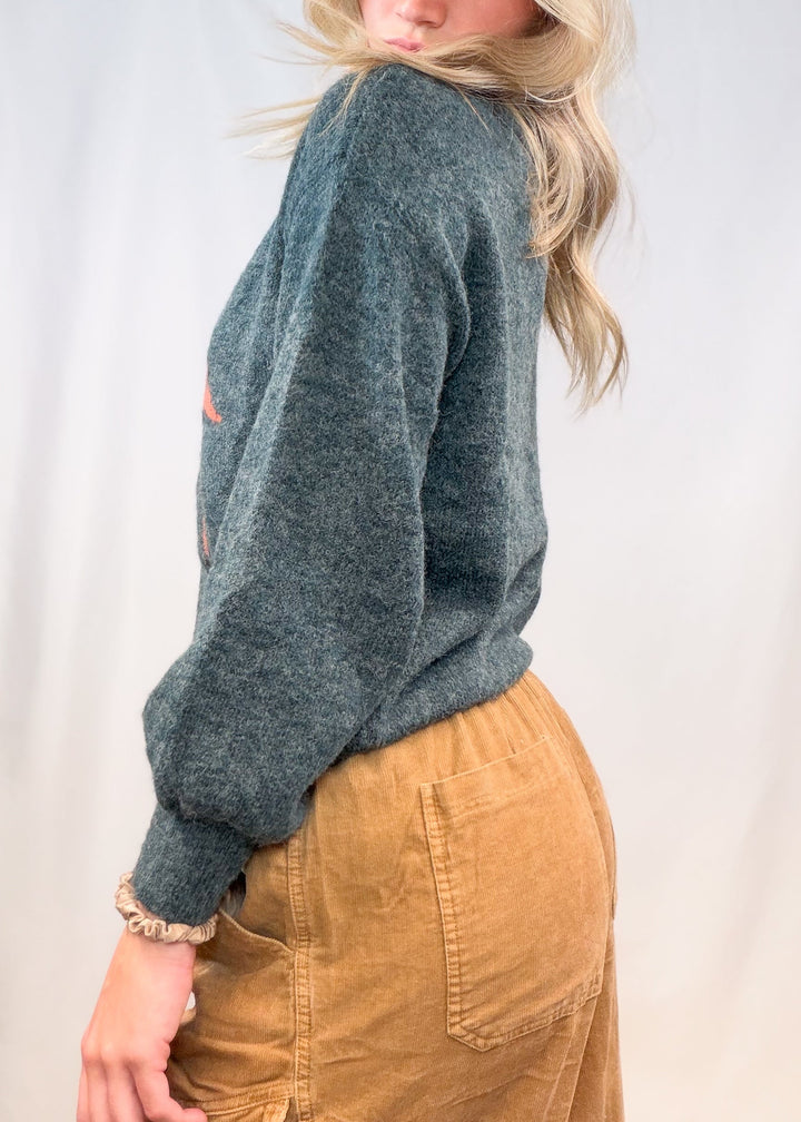 Woman wearing green sweater and corduroy pants on plain background