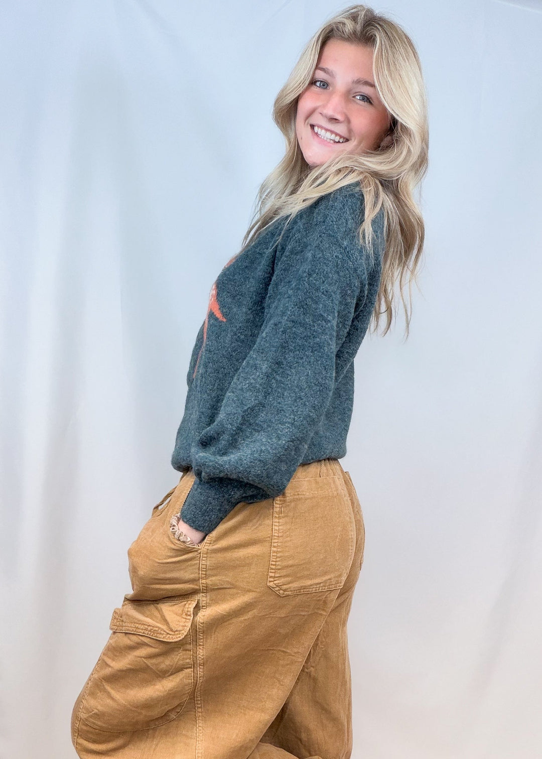Woman shown from side view wearing green sweater and corduroy pants on plain background