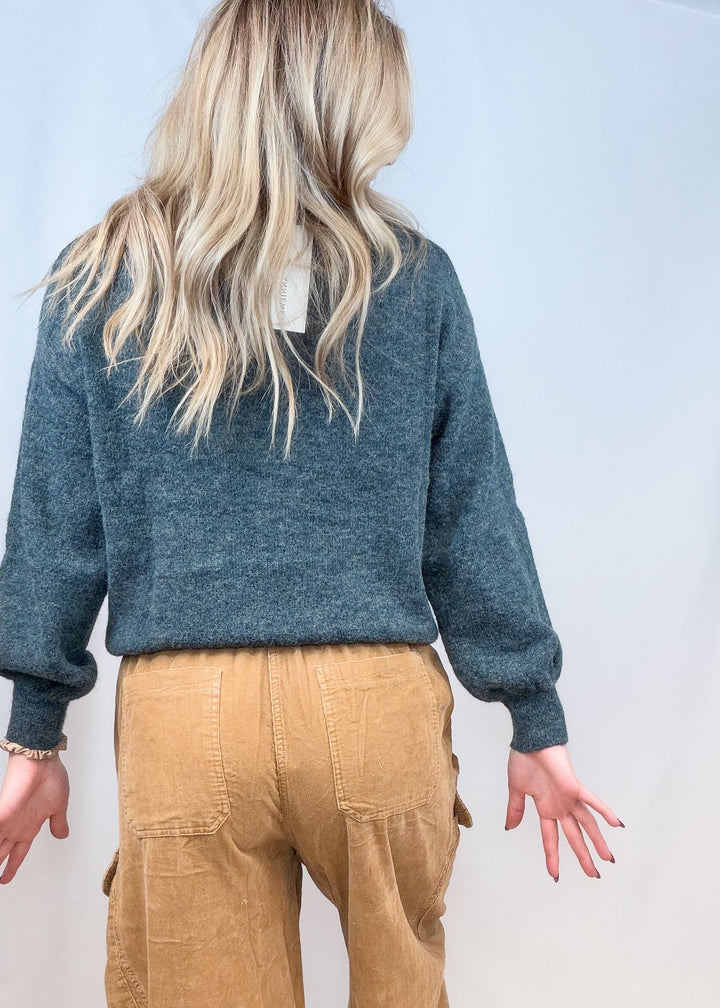 Woman shown from back view wearing green sweater and corduroy pants on plain background