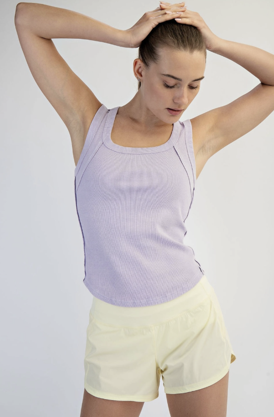 Woman wearing a light purple tank top and yellow shorts against a plain background