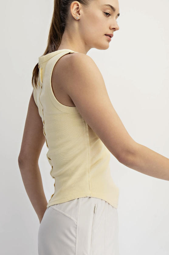 Woman wearing a light yellow sleeveless top against a plain background