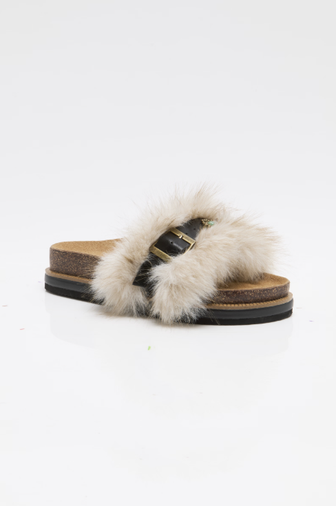 A single slide sandal with a fluffy cream fur strap, a black leather strap with a gold buckle, and a brown cork-look midsole on a white background.