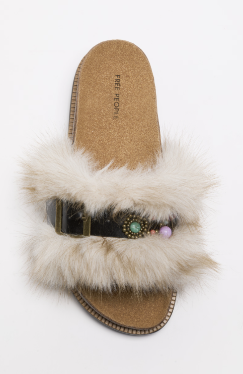 A single slide sandal with fluffy cream faux-fur trim, a black strap featuring a decorative turquoise and purple bead embellishment, and a tan cork-textured footbed. The brand name &