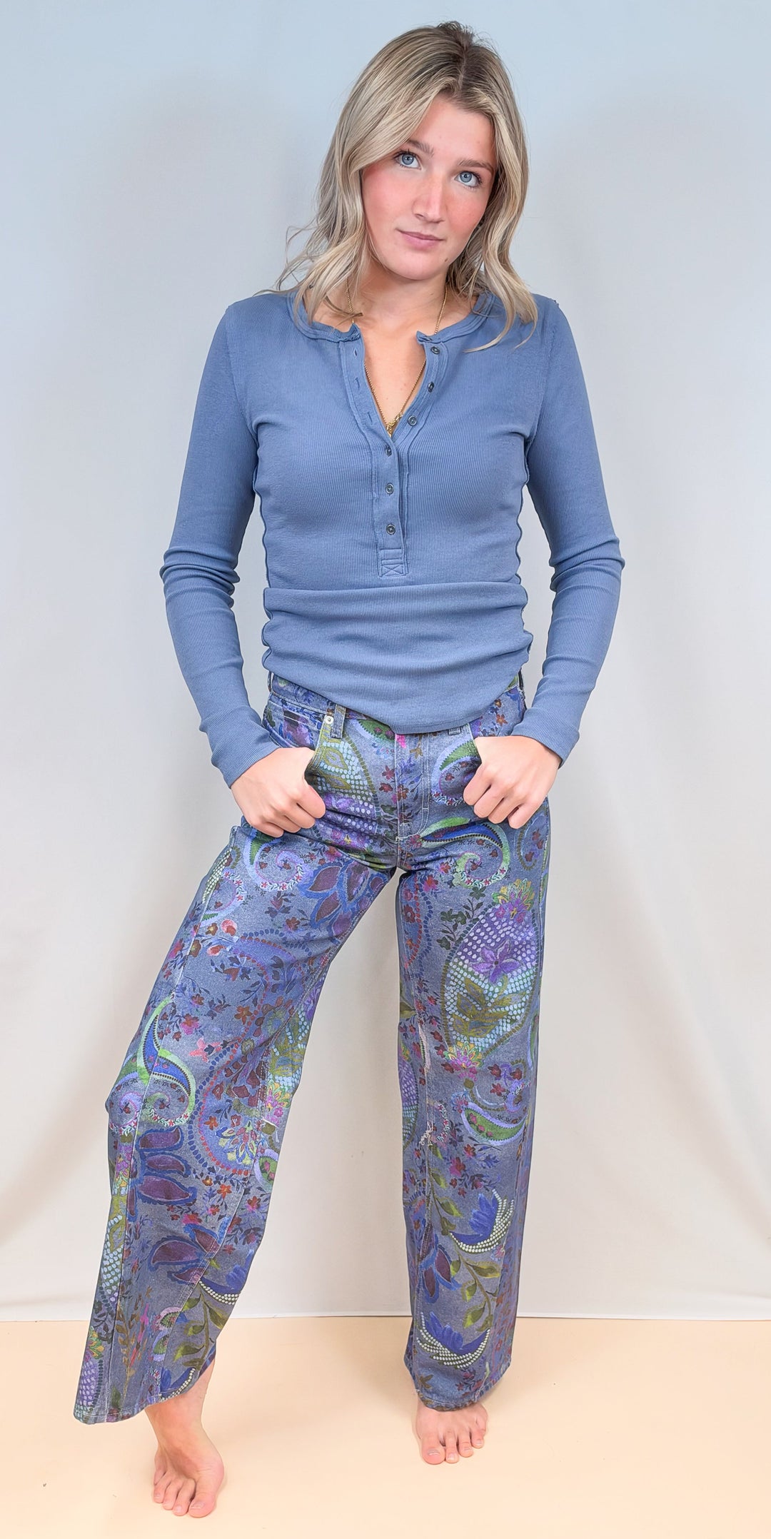 Woman wearing blue paisley jeans with blue long sleeve top on plain background