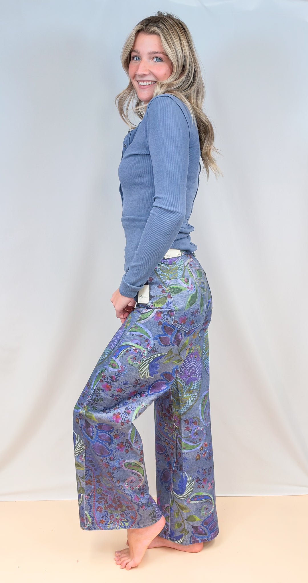 Woman shown from side view wearing blue paisley wide leg pants with blue long sleeve top on plain background