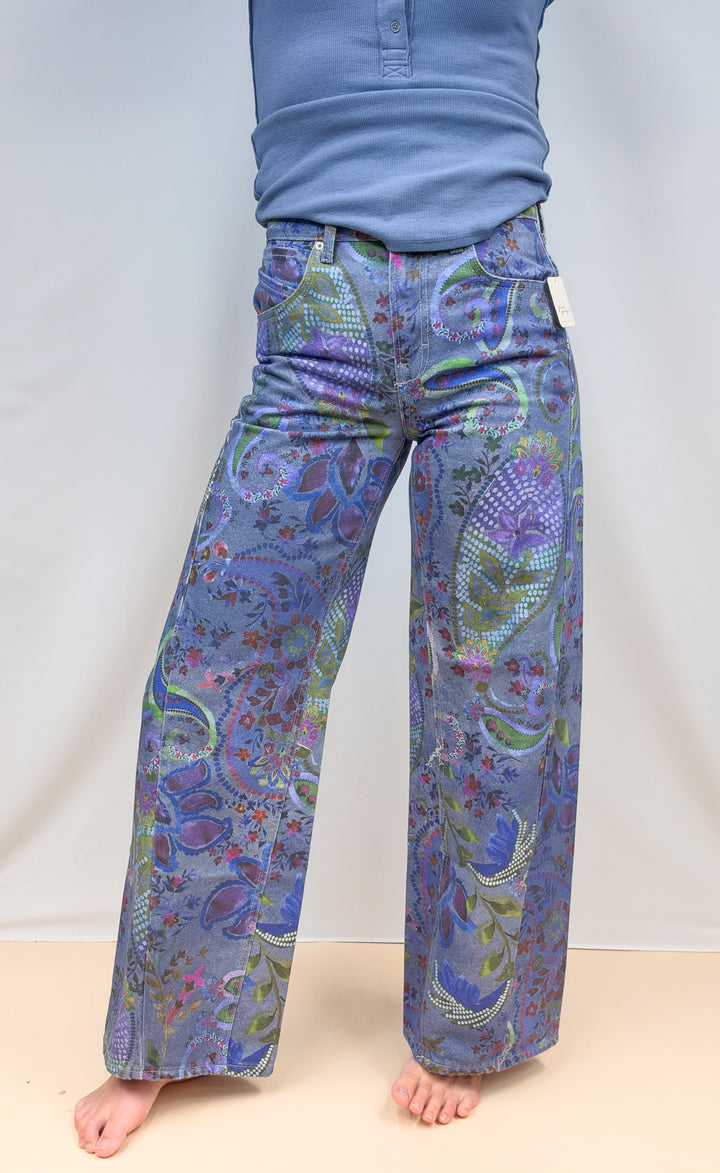 Woman shown from waist down wearing blue paisley jeans with blue long sleeve top on plain background