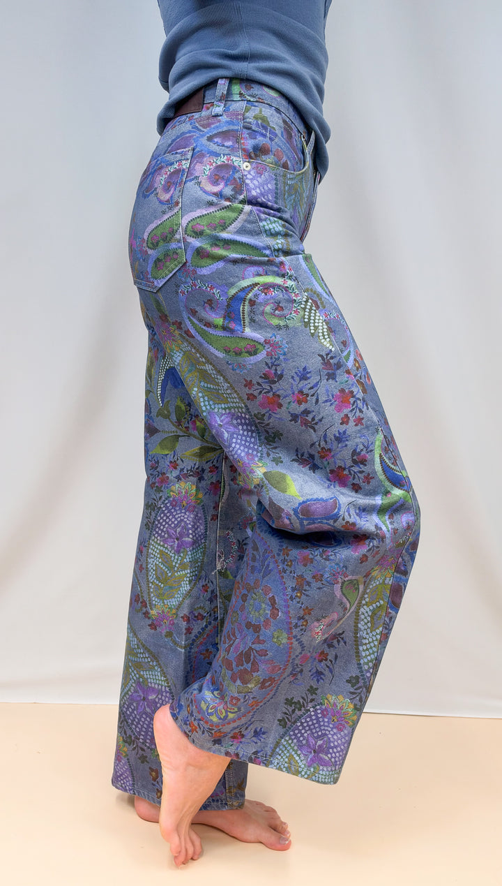 Woman shown from side view waist down wearing blue paisley jeans on plain background
