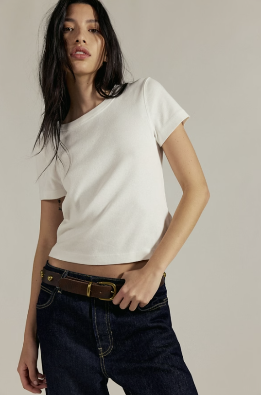 Woman wearing a white top and dark jeans against a plain background