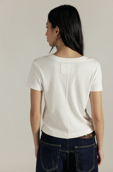Person wearing a white t-shirt and dark jeans against a neutral background